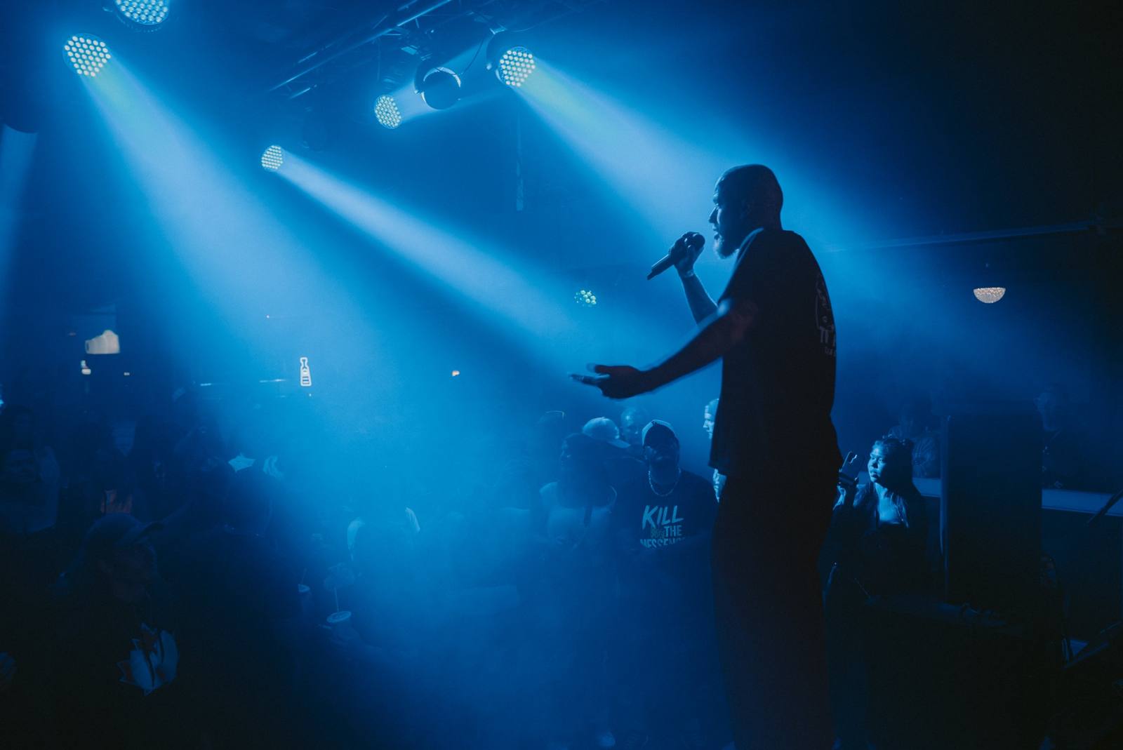 A performer on stage holding the mic out to the crowd under blue spotlights